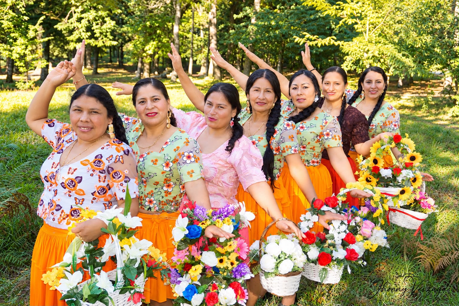 Cholitas levantan el brazo y sonríen con canastas de flores