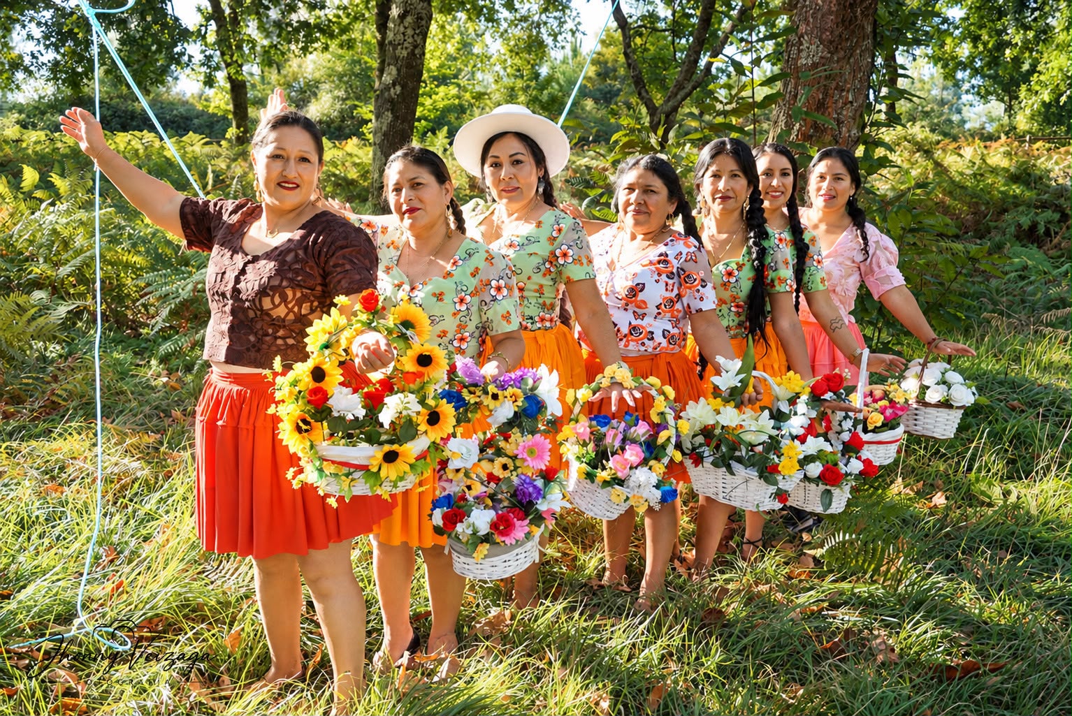 Cholitas posan en fila diagonal con canastas de flores en el parque
